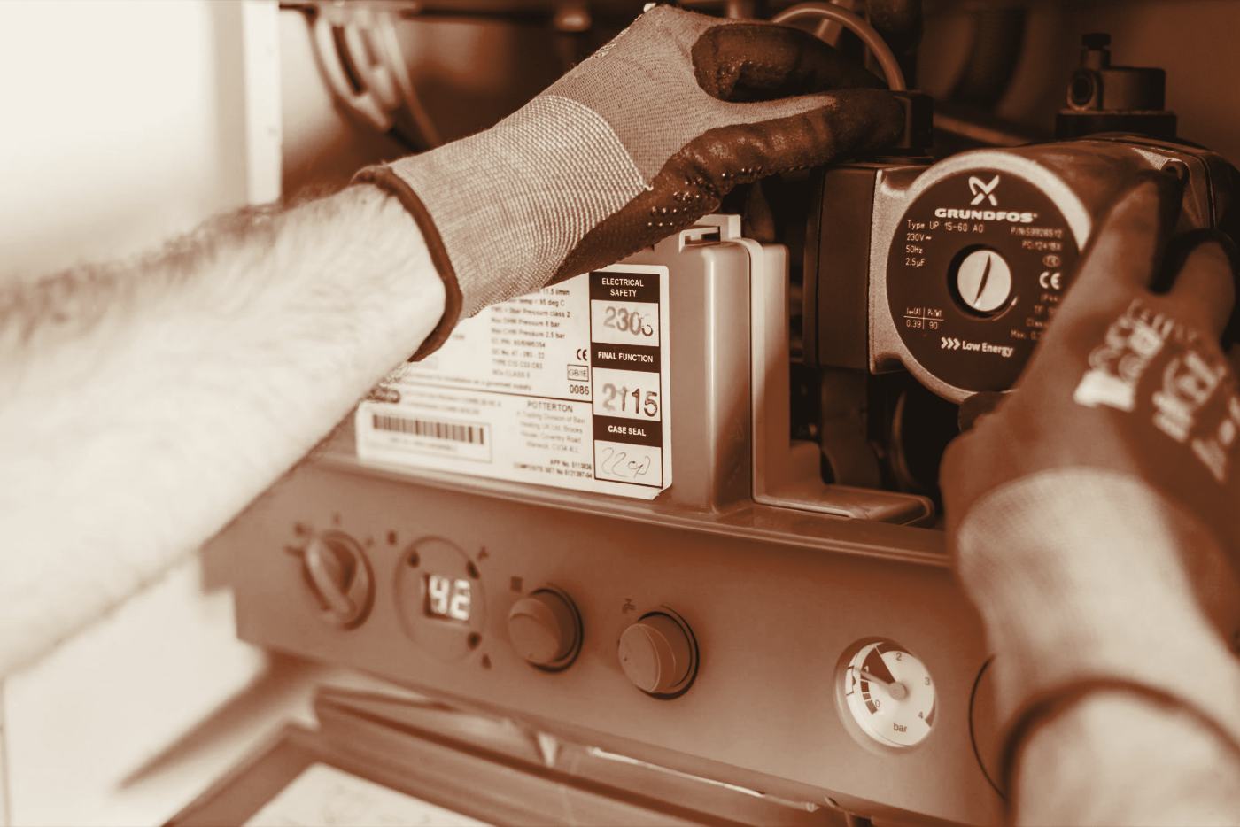 A Halloway Heating engineer working inside an open gas combi boiler, checking the pump and pressure gauge