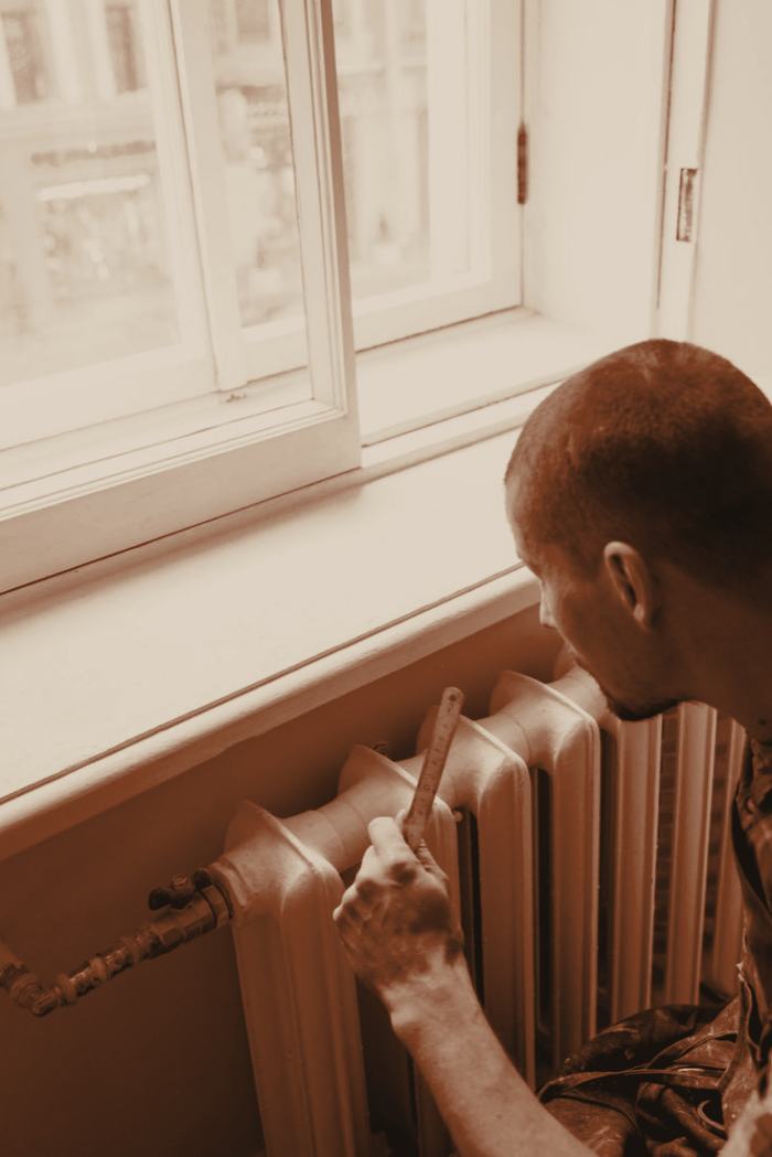An engineer measuring up an old cast iron radiator under a sash window